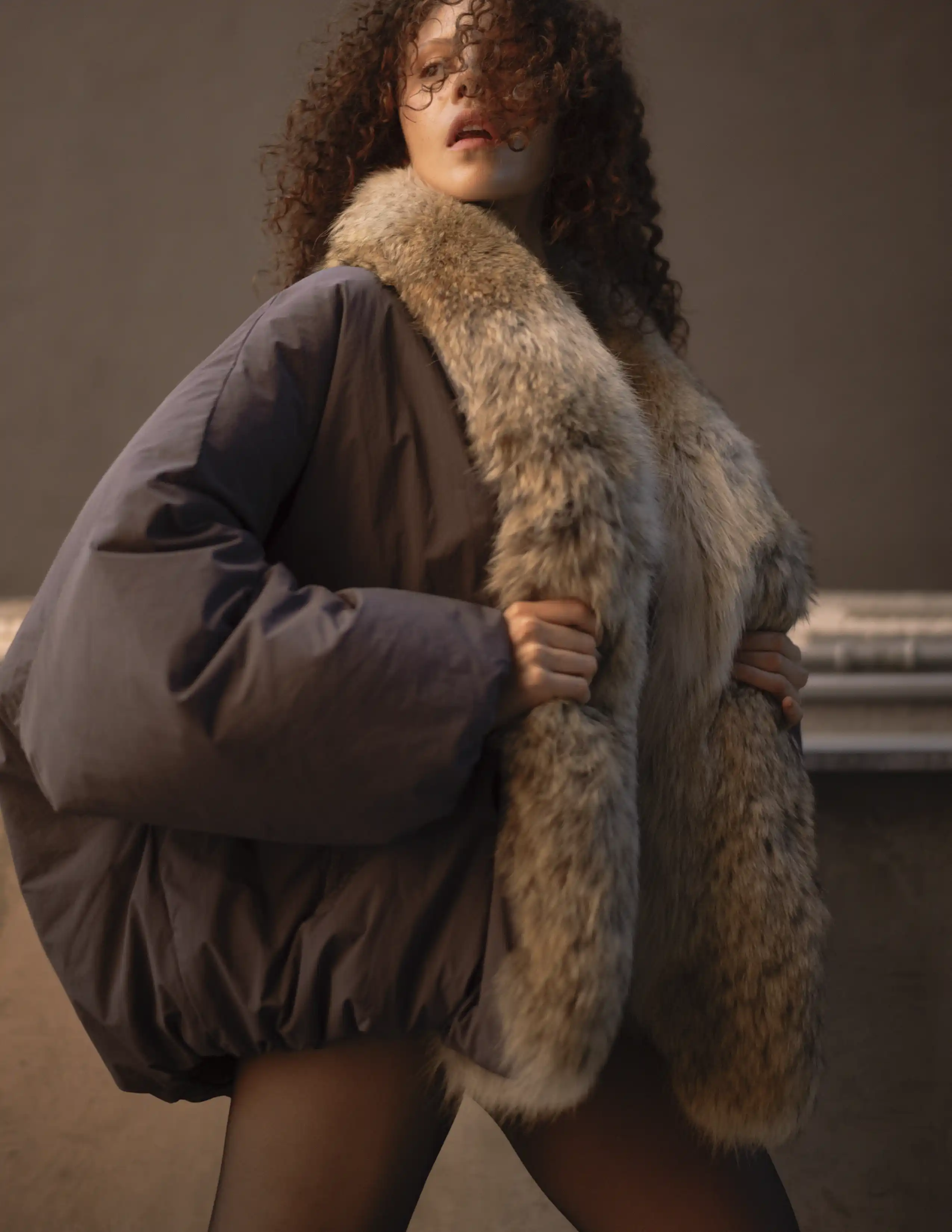 Modelo con abrigo oversized de piel sintética y mangas voluminosas en tonos grises, moda invierno editorial.